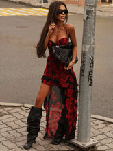 Woman in a red and black floral dress with black boots standing on a street.